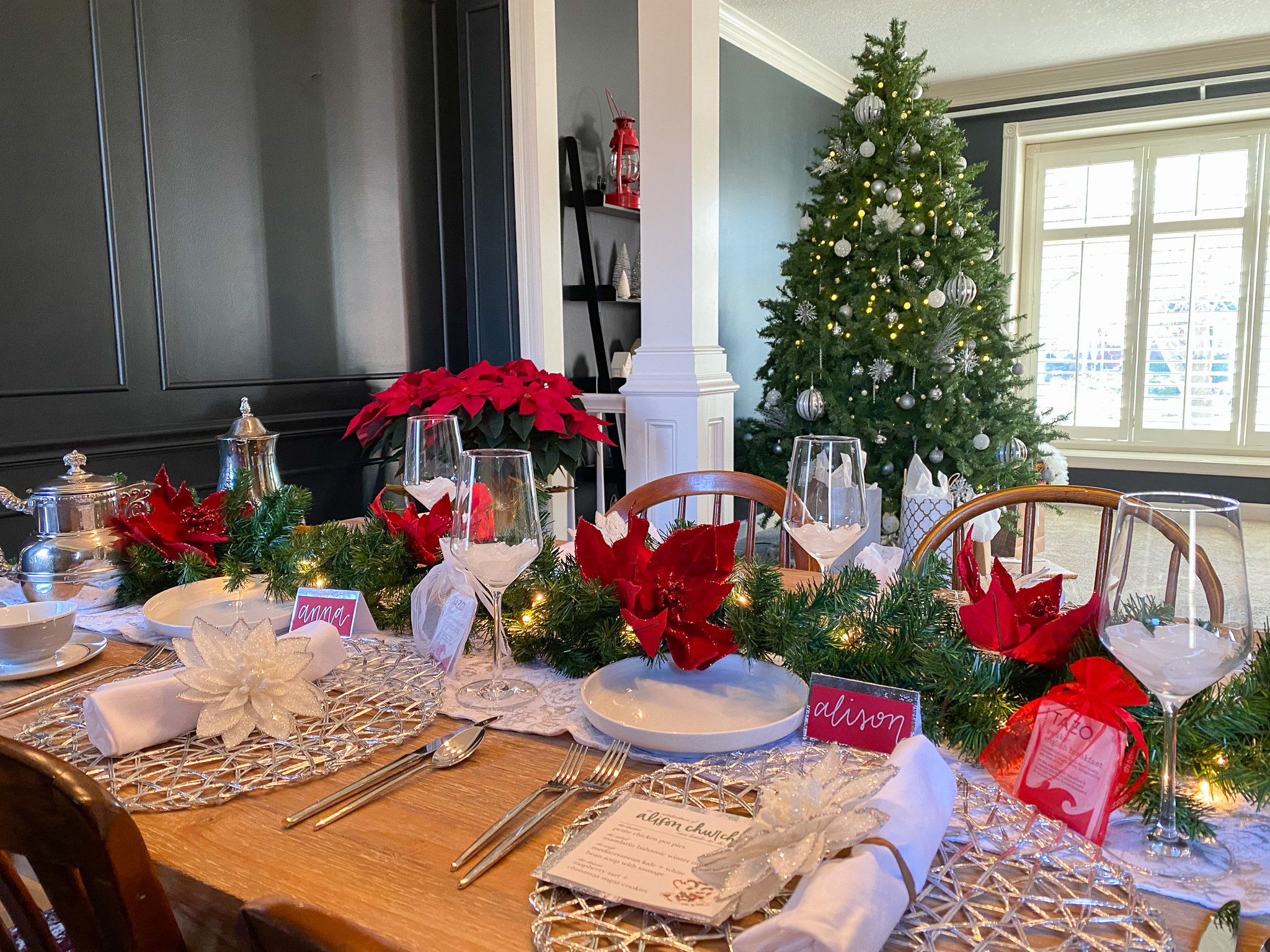 Christmas bridal shower table with red poinsettias, green garland, silver place settings and a decorated tree